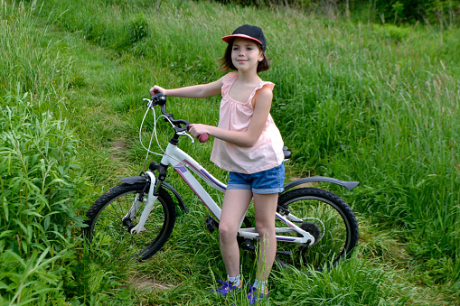 Young girl cyclist enjoy the beautiful sunrise on summer forest trail. Close-up portrait of a happy little girl in a helmet on a bicycle. High quality photo