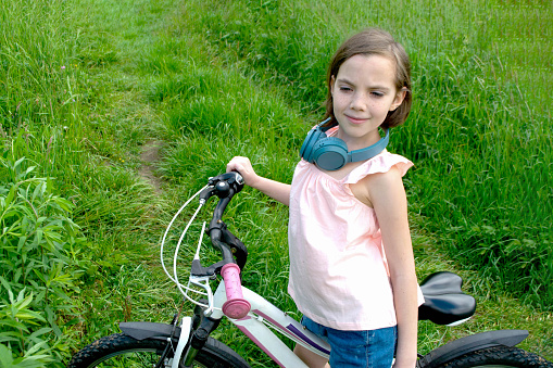 Young girl cyclist enjoy the beautiful sunrise on summer forest trail. Close-up portrait of a happy little girl in a helmet on a bicycle. High quality photo