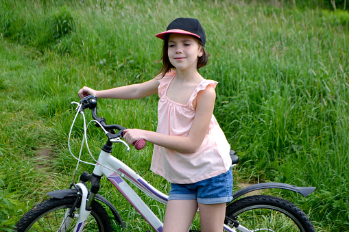 Young girl cyclist enjoy the beautiful sunrise on summer forest trail. Close-up portrait of a happy little girl in a helmet on a bicycle. High quality photo