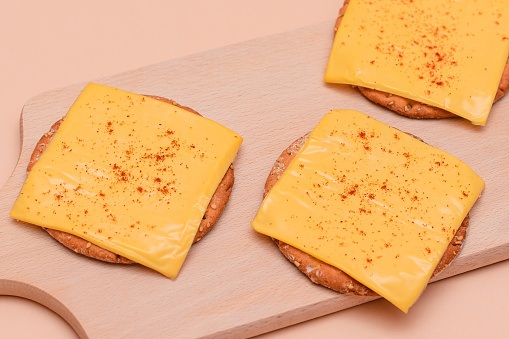 Crispy Cracker Sandwiches with Cheese and Paprika on Wooden Cutting Board and Beige Background
