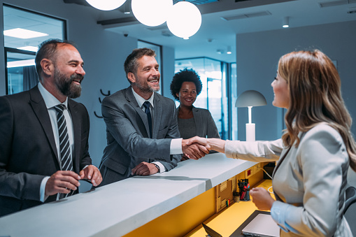 Shot of receptionist and businessman handshaking at hotel front desk.