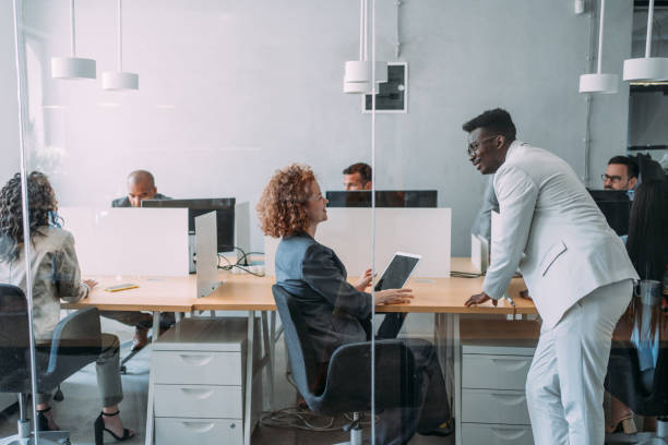 Business people working at a modern office. Shot of a group of business people sitting at their desks in a busy corporate office with open plan. The view is through glass. giant cube stock pictures, royalty-free photos & images