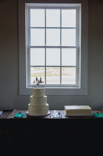 Vertical image of a three tier wedding cake with lots of detail and decoration. Large window in the background off center.