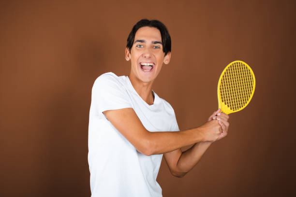 istock Funny guy with children's tennis rackets posing on a brown background. 1911524202