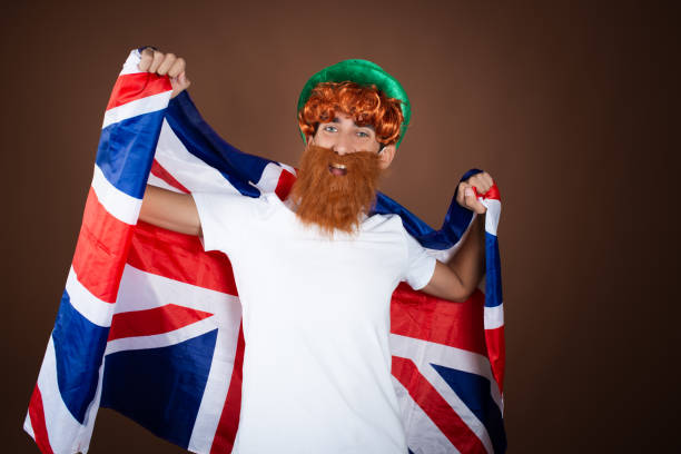 istock St.Patrick 's Day. Funny guy in a leprechaun costume posing on a brown background. 1911525148