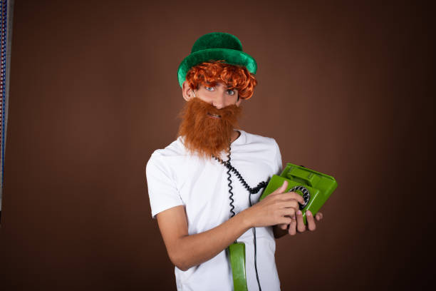 istock St.Patrick 's Day. Funny guy in a leprechaun costume posing on a brown background. 1911536602