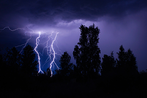 beautiful lightning during a thunderstorm at night in a forest that caused a fire, against a dark sky with rain