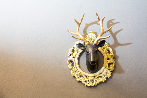 A black deer head sculpture with golden horns mounted on a gray wall.