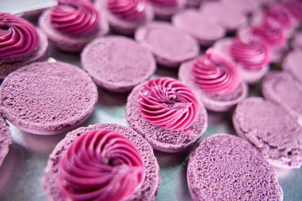 Closeup of purple macaron shells with cream filling on sheet pan placed on kitchen countertop