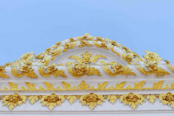 istock White cement gable with native golden flower pattern and clear sky. 1911587438