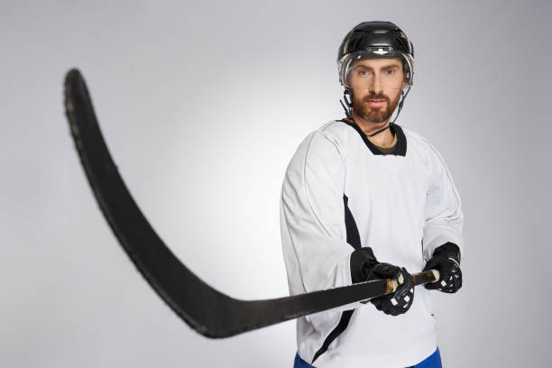 joueur de hockey sur glace portant un casque pointant un bâton noir vers la caméra. - adult isolated color image studio shot photos et images de collection