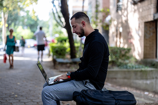 In a serene public park, a young businessman works attentively on his laptop, blending nature with productivit