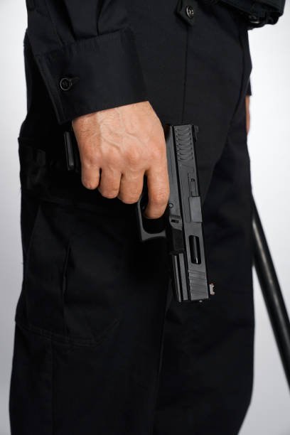 istock Anonymous man in uniform carrying handgun, firearm, with forefinger on trigger. 1911615470