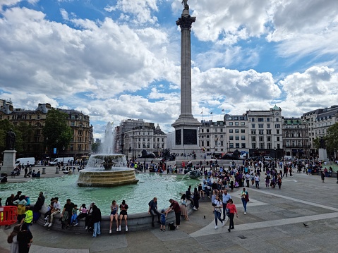 Trafalgar Square is a public square in the City of Westminster, Central London, established in the early 19th century around the area formerly known as Charing Cross. the image shows the square with tourists captured during summer season.