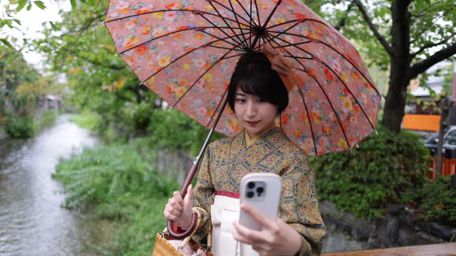 Young woman in Kimono / Hakama taking selfie picture on bridge - slow motion