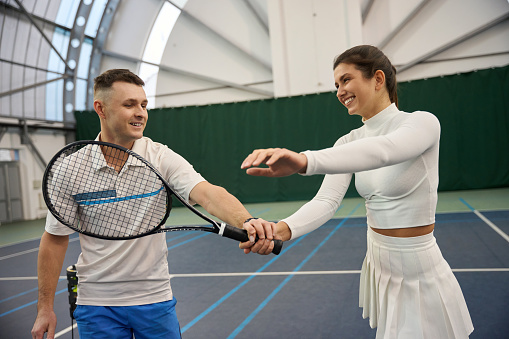 Confident man teaching woman to properly hold paddle racquet during training on indoor tennis court