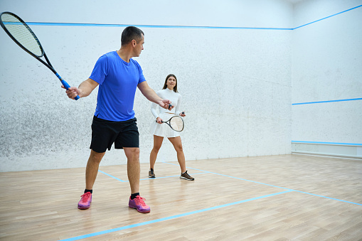 Man instructor fervently teaching woman to play squash exercising on indoor court