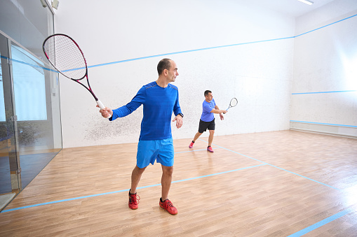 Sporty men playing squash showing their athletic skills on indoor court