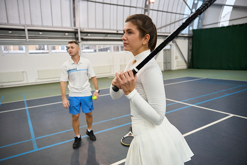 Man instructor helps woman learn tennis they practice hitting ball on indoor court