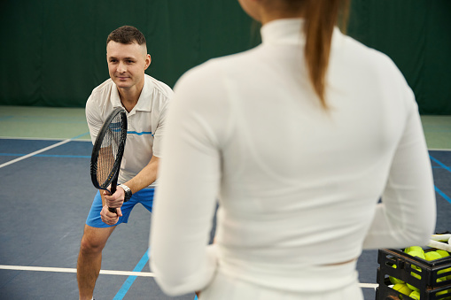 Man trainer teaching woman to hit ball effectively in their tennis workout on indoor court
