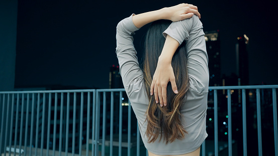 Healthy young Asian woman warming up and stretching before exercise on sky running track on high building in city at night, Healthy lifestyle with exercise activities, Outdoor fitness at night, City lifestyle with workout