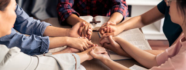 Believer hand praying together on bible book while holding hand. Burgeoning Cropped image of diversity people hand praying together at wooden church on bible book while hold hand together with believe. Concept of hope, religion, faith, god blessing concept. Burgeoning. christianity stock pictures, royalty-free photos & images