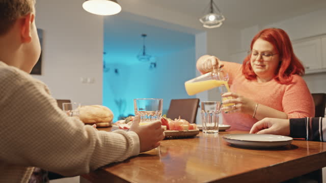 Happy Mother Serving Juice in Glasses While Having Dinner with Family at Home