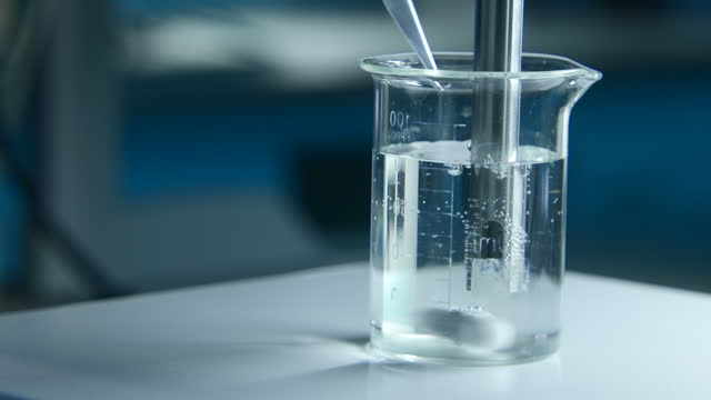 Rotating substance in glass of liquid in laboratory. Stock footage. Chemical experiment with substance and liquid in flask. Professional chemical experiment in laboratory.