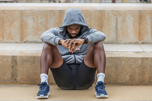 Full body of young upset African American male athlete sitting with head down on ground failure and depression concept
