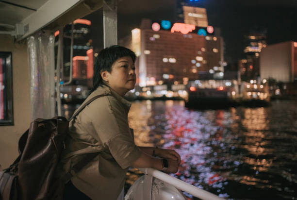asian chinese mature woman taking star ferry crossing hong kong island to kowloon at night - sailing light wind nautical vessel imagens e fotografias de stock