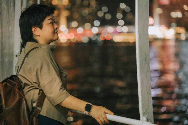 asian chinese mature woman taking star ferry crossing hong kong island to kowloon at night - sailing light wind nautical vessel imagens e fotografias de stock