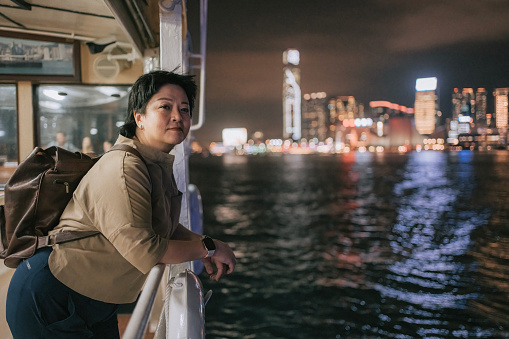 Asian Chinese mature woman taking star ferry crossing Hong Kong Island to Kowloon at night