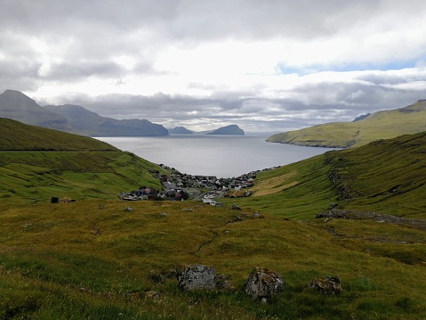 A small village in a valley by the Atlantic Ocean in the Faroe Islands on a cloudy summer day. In the surroundings, green pastures full of moss and fresh grass