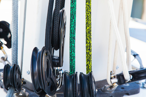 Part of the mast and hull of a sailing yacht, with multi-colored ropes, rollers and hinges for securing sails.