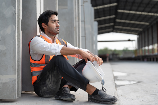 Asian man civil engineer feel tired and stressed from working outdoor at factory or construction site making precast concrete wall for real estate housing.