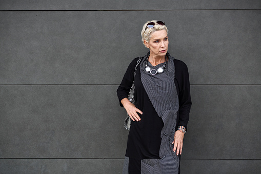 Mature woman standing at a gray wall. Senior female portrait.