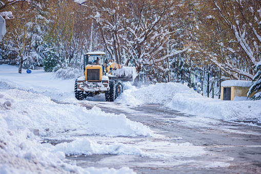 In heavy snow, a snowplow is clearing snow on the street.