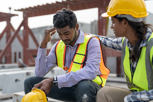 Asian Indian man worker feeling sad and upset while sitting at construction site. Female worker colleague supporting and consolation him.