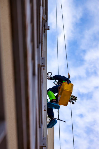 istock Rope access laborer hanging from wall residential building during high-rise work. Bottom view of industrial mountaineer worker in work uniform. Industry urban works concept. Copy ad text space 1911768525