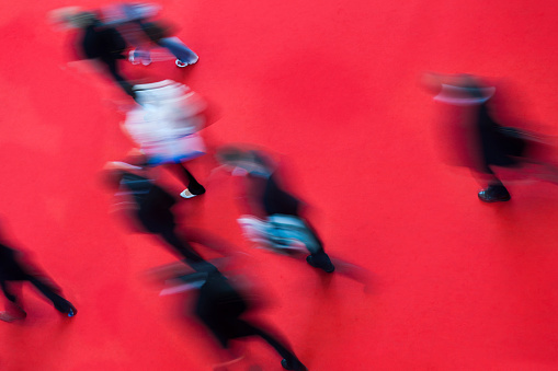 Group of motion blurred people walking in different directions on red carpet in modern hallway.