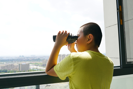 kid with telescope watching outdoor near window
