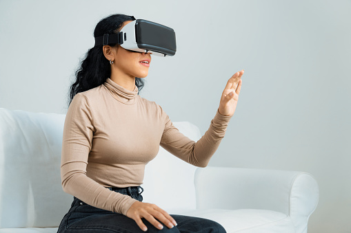 Young woman using virtual reality VR goggle at home for crucial online shopping experience. The virtual reality VR innovation optimized for female digital entertainment lifestyle.