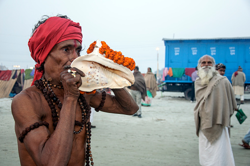 South 24 parganas, west Bengal. A devotee blowing traditional conch shell at Gangasagar religious fair in afternoon.