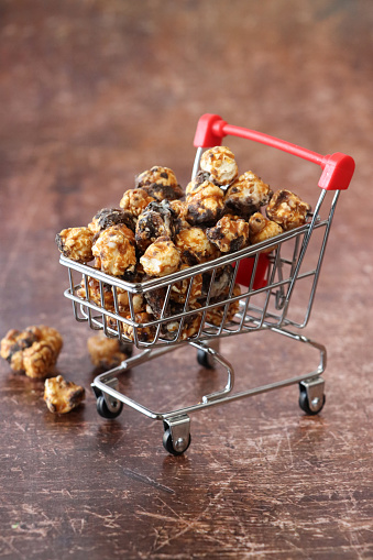 Stock photo showing close-up view of heap of chocolate covered popped corn kernels in a miniature, model shopping trolley. Unhealthy eating concept.