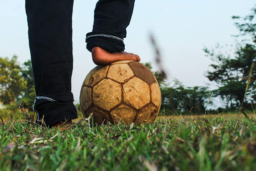 Child's foot steps on ball on green grass