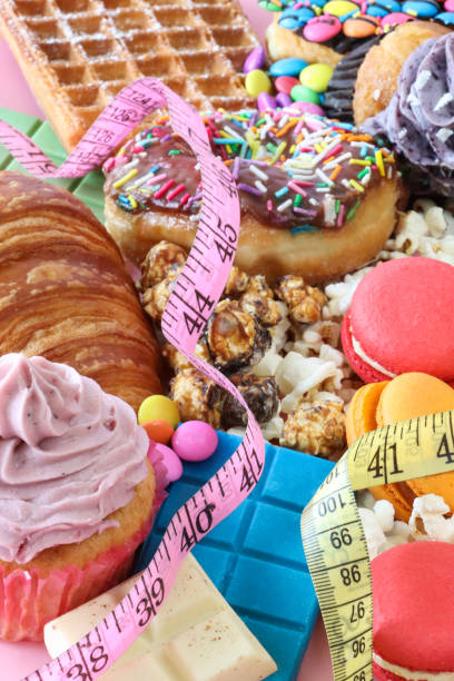 Stock photo showing close-up image of a variety of sweet junk food items including glazed ring doughnuts, popcorn, waffle, cupcakes with butter icing, macarons, croissant, chocolate bars, Smarties candy coated chocolate sweets. Unhealthy eating concept. imagen de fotograma completo de cintas métricas en comida chatarra dulce, rosquillas de anillo glaseadas, palomitas de maíz, gofres, magdalenas con glaseado de mantequilla, macarons, croissant, barras de chocolate, dulces de chocolate recubiertos de cara