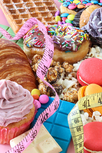 Stock photo showing close-up image of a variety of sweet junk food items including  glazed ring doughnuts, popcorn, waffle, cupcakes with butter icing, macarons, croissant, chocolate bars, Smarties candy coated chocolate sweets. Unhealthy eating concept.