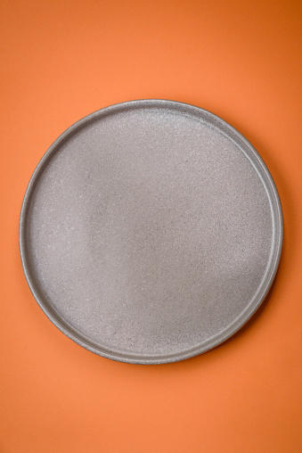 Empty round ceramic plate on a plain background, flatley with copy space. Kitchen utensils in home kitchen