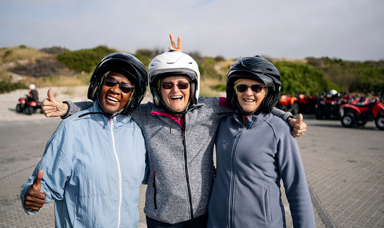 Group of three senior female friends with helmets showing thumbs up before riding quadbikes on their vacation