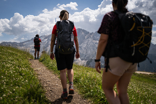 Group of friends trail hiking on a Dolomites trail, in Italy, during summer vacations. They are on the Viel del Pan famous trail, from Passo Pordoi to Fedaia pass